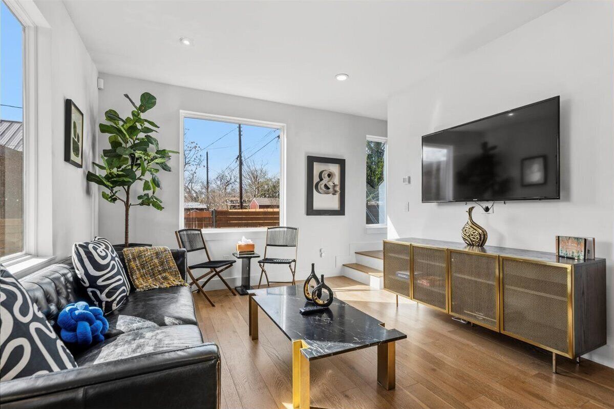 A modern living room with a black leather sofa, a glass coffee table, and a black TV on the wall.