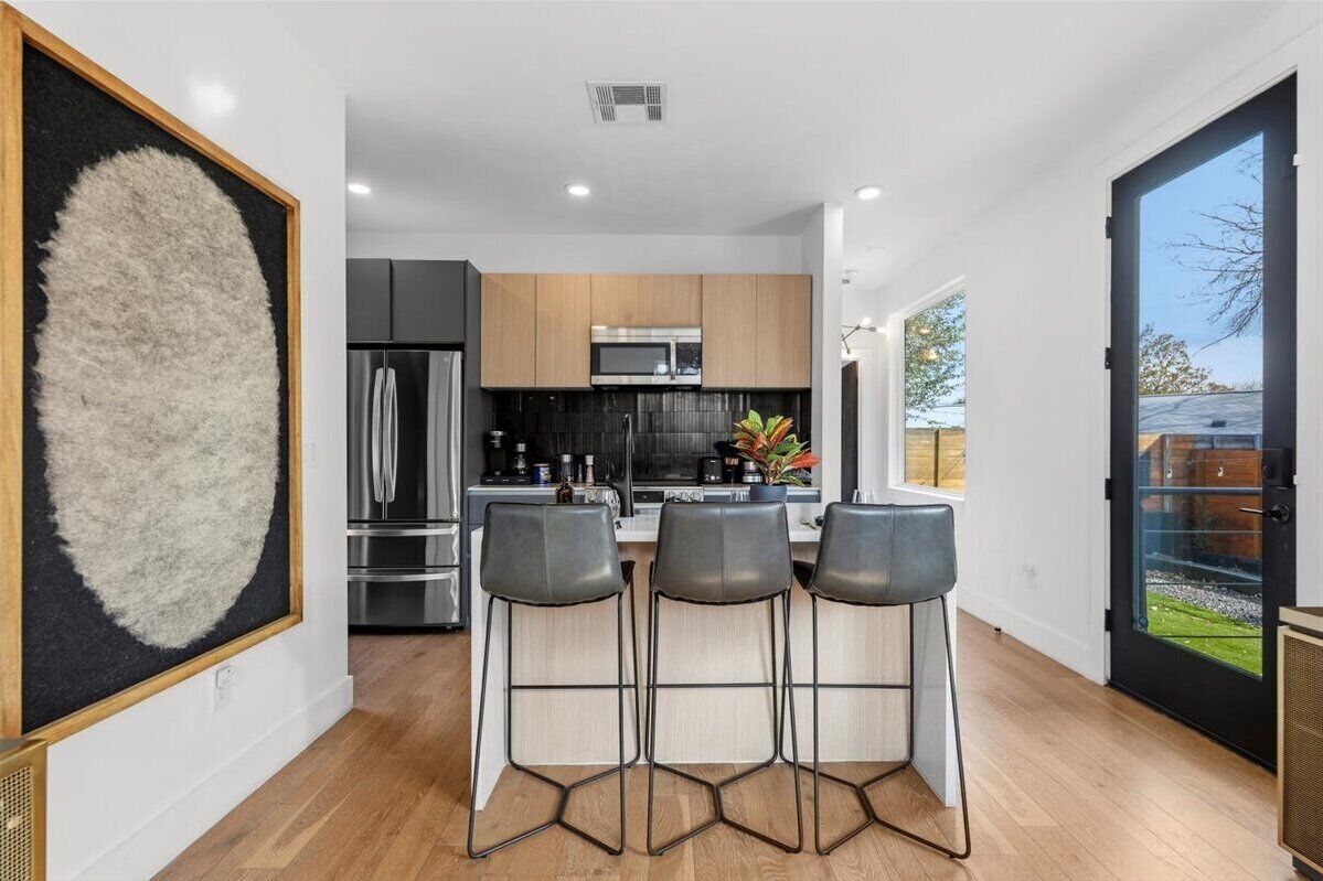 A modern kitchen with a central island, stainless steel appliances, and a large window offering a view of the outdoors.