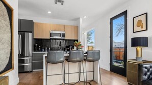 A modern kitchen with stainless steel appliances, a wooden countertop, and three bar stools. - Gladeview Dr (Austin)