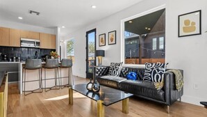 A modern living room with a black leather sofa, a coffee table, and a kitchen in the background. - Gladeview Dr (Austin)