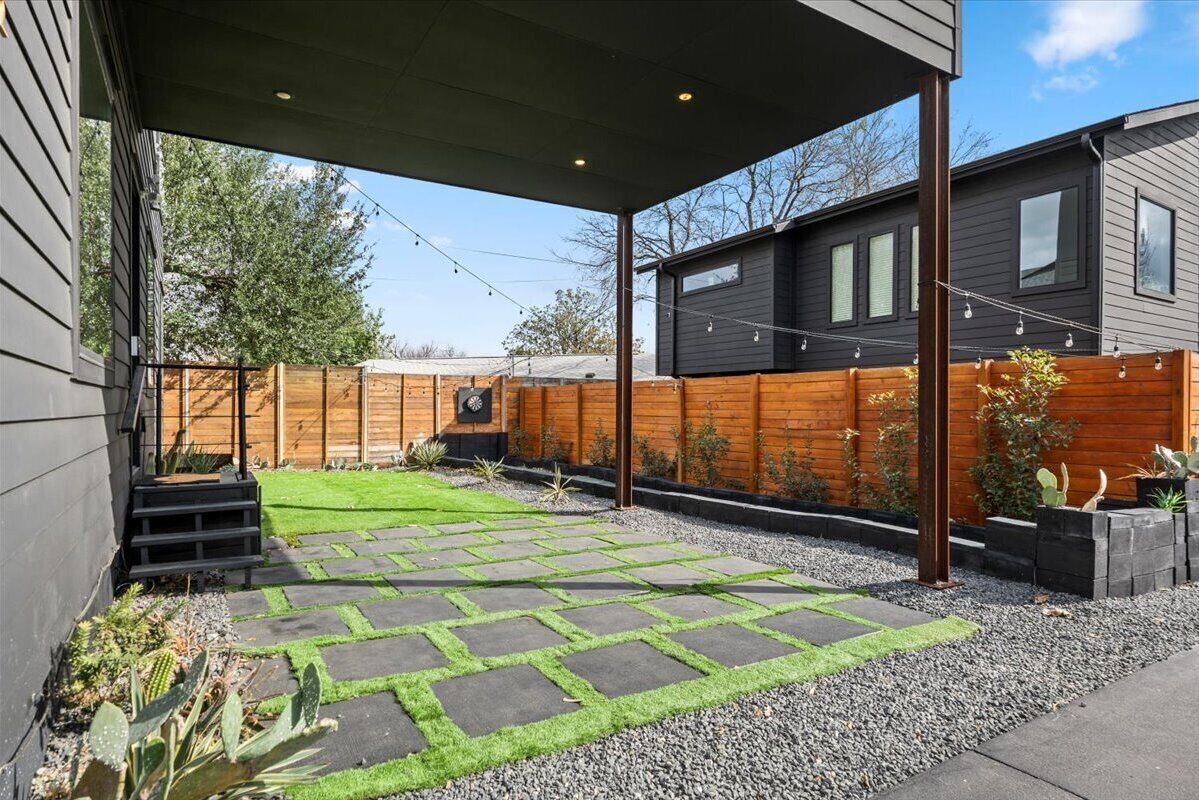 A modern backyard with a stone patio, a wooden fence, and a small garden area.