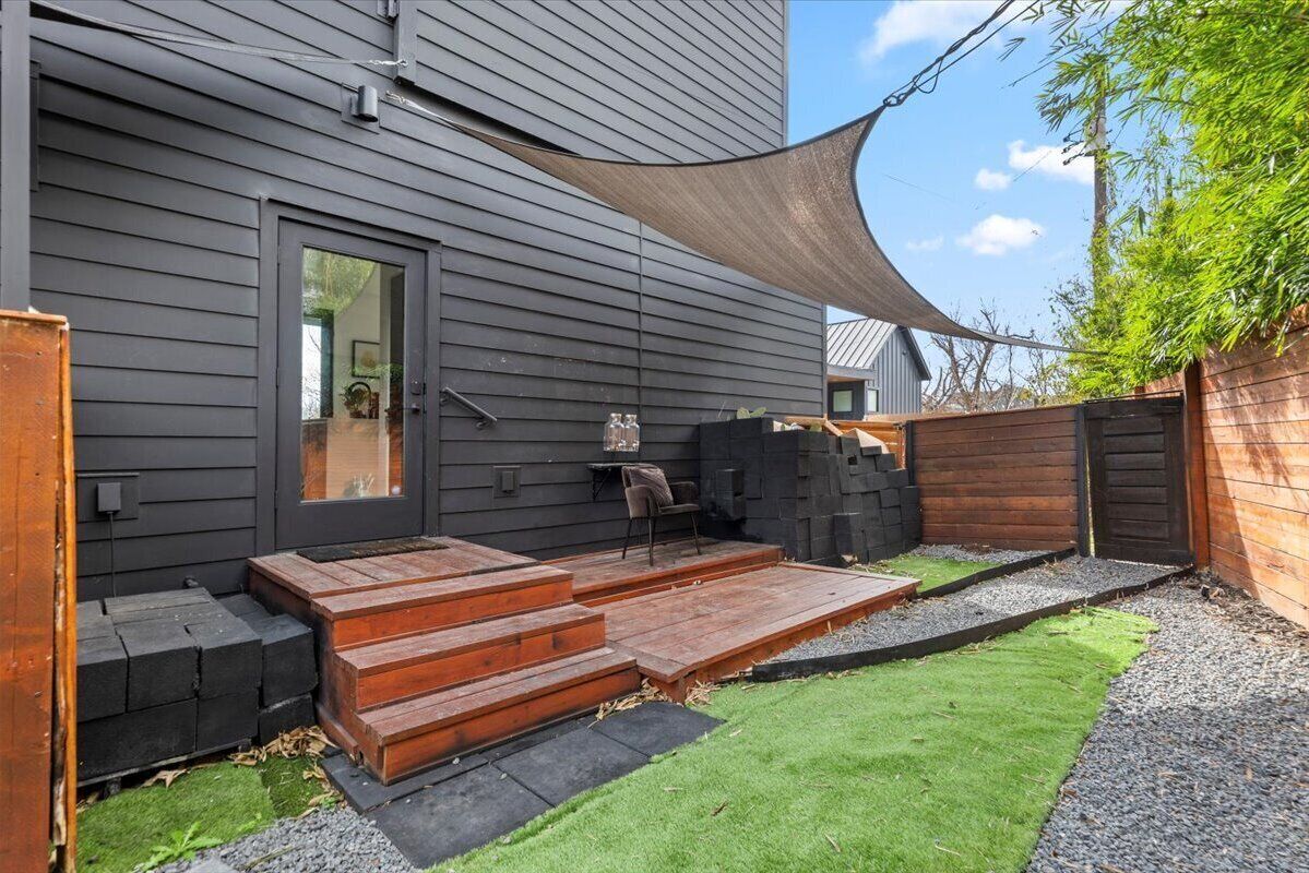 Una casa moderna amb façana fosca, un terraço de fusta i un jardí en verd.