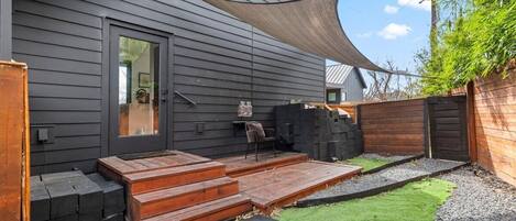 Una casa moderna amb façana fosca, un terraço de fusta i un jardí en verd.