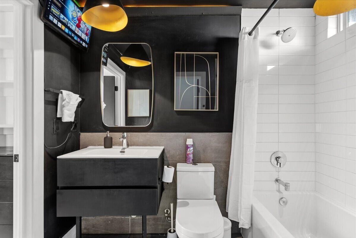 Un baño moderno con una paleta de colores blanco y negro, que incluye un lavamanos, inodoro y ducha.