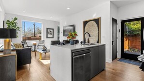 A modern kitchen with a central island, a dining area with a sofa and table, and a view of the outdoors. - Gladeview Dr (Austin)