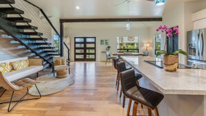Una cocina amplia con una isla central, un comedor con sillas, una escalera y una sala de estar con sofá y sillones.