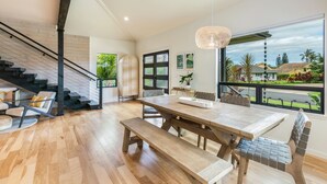 Un amplio salón con piso de madera, una gran mesa de comedor con bancos, una escalera y un ventanal que ofrece vistas al exterior.