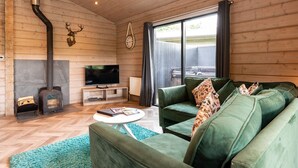 Una sala de estar acogedora con chimenea, sofá verde, televisor de pantalla plana y un amplio ventanal con cortinas.