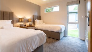 Un dormitorio moderno con dos camas, una mesita de noche, una lámpara y una ventana con vistas al exterior.