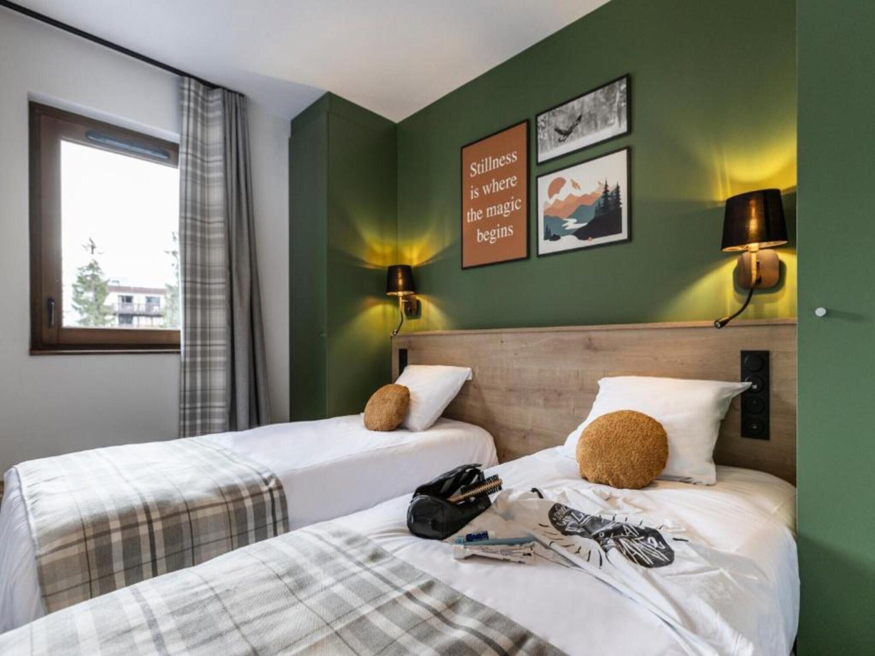 Ein Hotelzimmer mit zwei Betten, einem Fenster mit Vorhängen, einer Wand mit motivierenden Postern und einem Nachttisch mit Lampe.