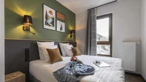 Een hotelkamer met een bed, twee wandlampen, een raam met uitzicht en een radiator.