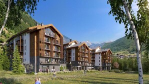 Een modern hotel met meerdere verdiepingen, grote ramen en een natuurlijke omgeving met bomen en bergen op de achtergrond.