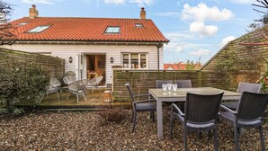 Een huis met een rode pannendak, een terras met rieten meubels en een grindpad.