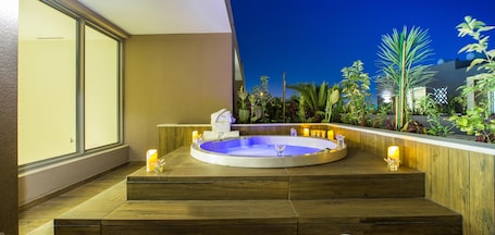 A hot tub with a wooden deck and steps, surrounded by plants and a night sky view.
