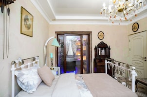 Een slaapkamer met een bed, een kroonluchter, een houten dressoir en een deur die leidt naar een balkon.