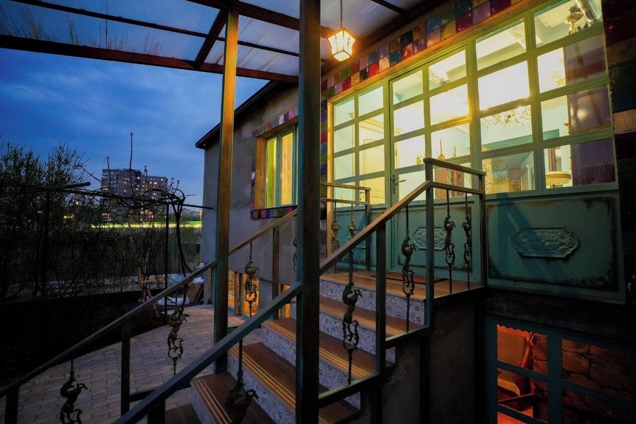 Una escalera con barandillas metálicas ornamentales y vista a un edificio con ventanas amplias y una puerta verde.