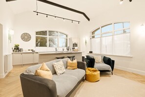 A modern living room with a sofa, two armchairs, and a coffee table. A kitchen with a large window and a dining area are visible in the background. - The Reading Room - North East Escapes (Shilbottle)