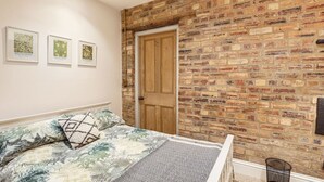 Ein Schlafzimmer mit einer Ziegelwand, einer Holztür und einem Bett mit gemusterten Betttextilien.