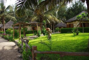 A tropical resort with thatched-roof cottages, a wooden pergola, and a well-maintained lawn. - AFRICA ROOTS (Lompoul)