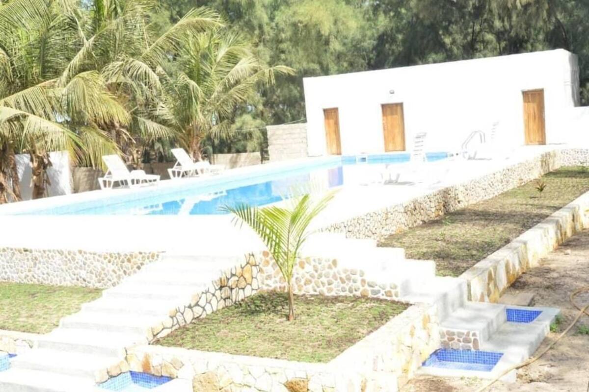 Un espace piscine avec des marches menant à l’eau, entouré de palmiers et d’un bâtiment blanc doté de portes.