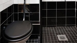 Casa de banho com sanita, uma pia preta e chuveiro com torneira cromada.
