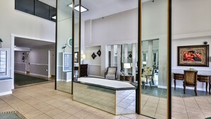 A spacious hotel lobby with a reception desk, a seating area with chairs, and a large mirror reflecting the space. - Feel the Sea Breeze, Stylish 2 BR Condo on the Beach W/ Pool (Daytona Beach)