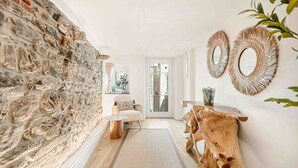 Un pasillo con pared de piedra, una mesa de madera, un sofá y dos espejos colgados en la pared.