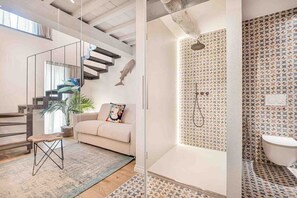 A modern interior with a staircase, a sofa, a small wooden stool, and a shower area with patterned walls. - asa Tre Uliva – The Elegance of Silence, the Luxury of the GenuineIn the most authentic heart of Corniglia, Casa Tre Uliva comes to life in 2025: a high-end guesthouse that redefines the concept of hospitality in the Cinque Terre. Four charming rooms,  (Corniglia)