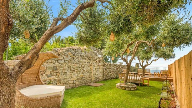 Un muro de piedra, un sofá de mimbre y una terraza de madera en un jardín.