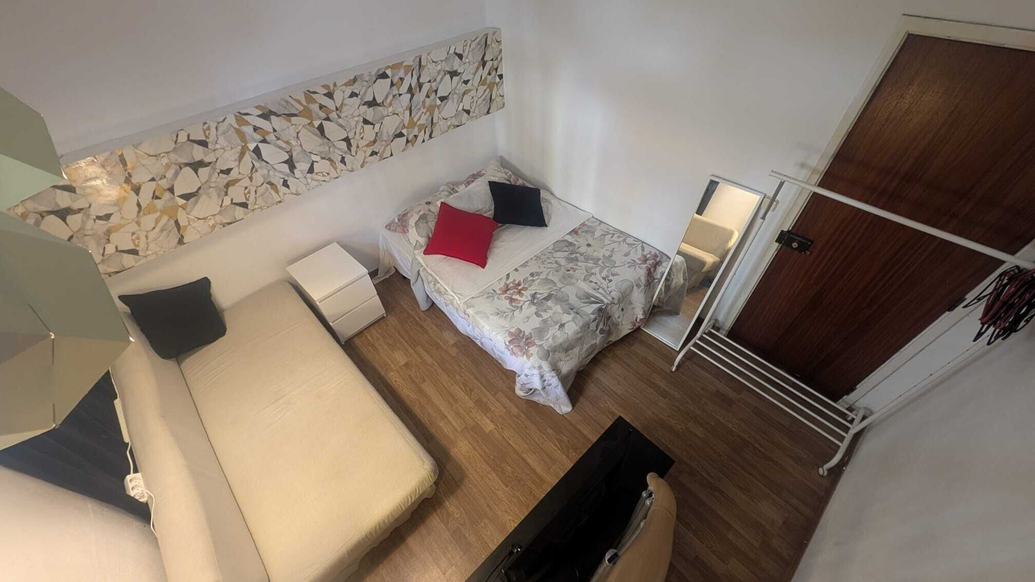A compact room with a bed, a small bedside table, a mirror, and a wardrobe.