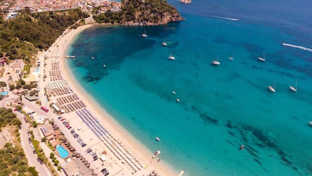 Une vue aérienne d’une ville côtière avec une plage, des bateaux et une petite île.