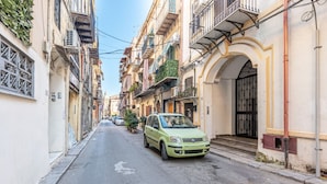 Una calle estrecha flanqueada por edificios de varios pisos, con balcones y pequeñas plantas.