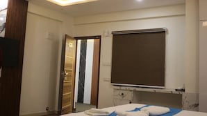 A modern hotel room with a bed, a television, a ceiling fan, and a large mirror. - Niharika Heights Luxury Hotel (Bengaluru)
