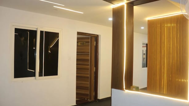 A modern hallway with a large mirror, recessed lighting, and a door with a number sign. - Niharika Heights Luxury Hotel (Bengaluru)
