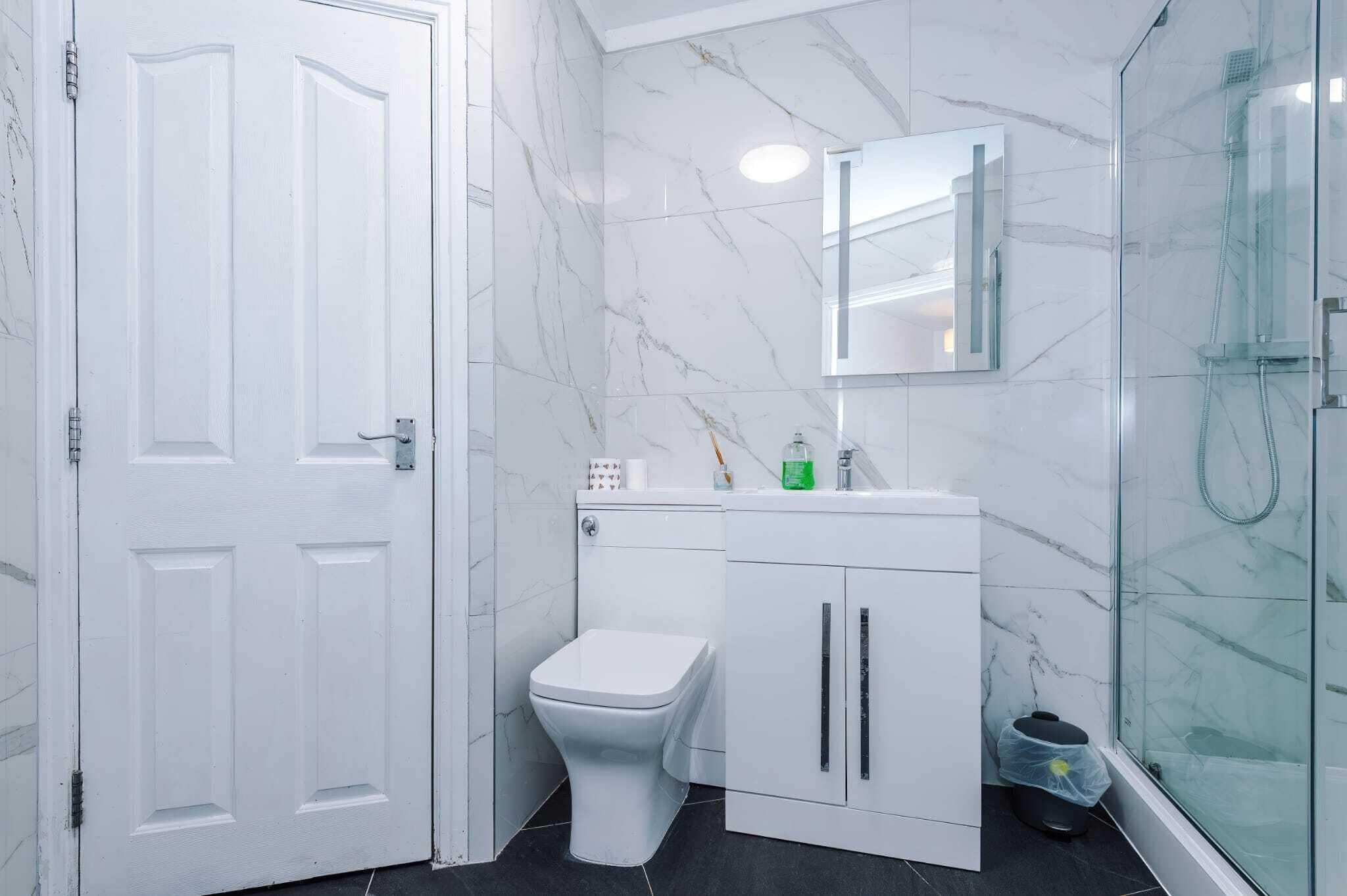 A bathroom with a toilet, sink, mirror, and shower.