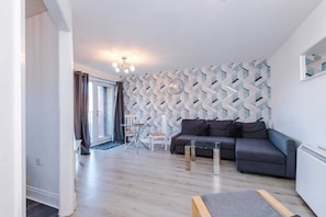 Un salon moderne avec un canapé gris, une table basse en verre et un mur orné d’un motif.