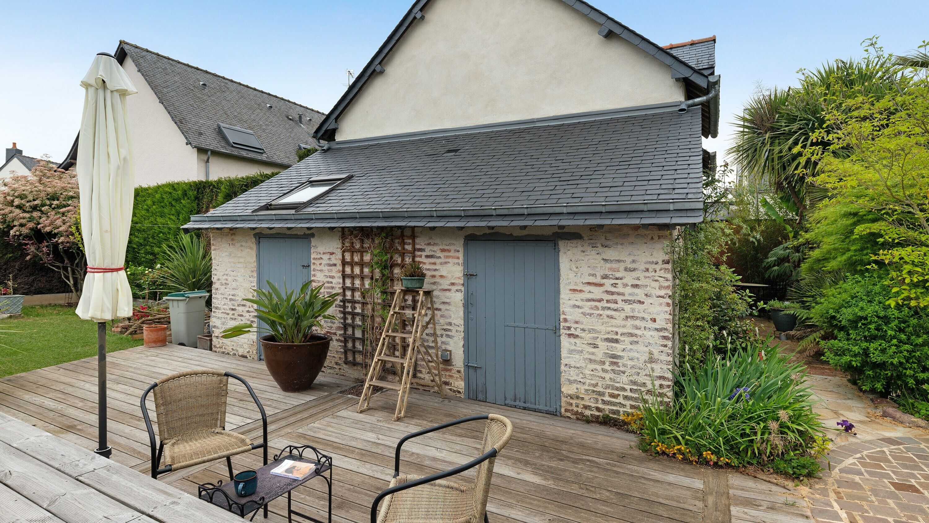 Une maison avec une terrasse en bois, une porte bleue et une plante en pot.