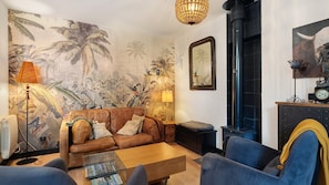 Un salon avec un canapé en cuir marron, une table basse, une lampe, un tableau, une cheminée et une fresque murale aux motifs tropicaux.