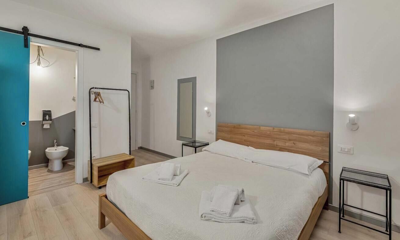 A modern hotel room with a large bed, a bedside table, a mirror, and a bathroom with a toilet and sink.