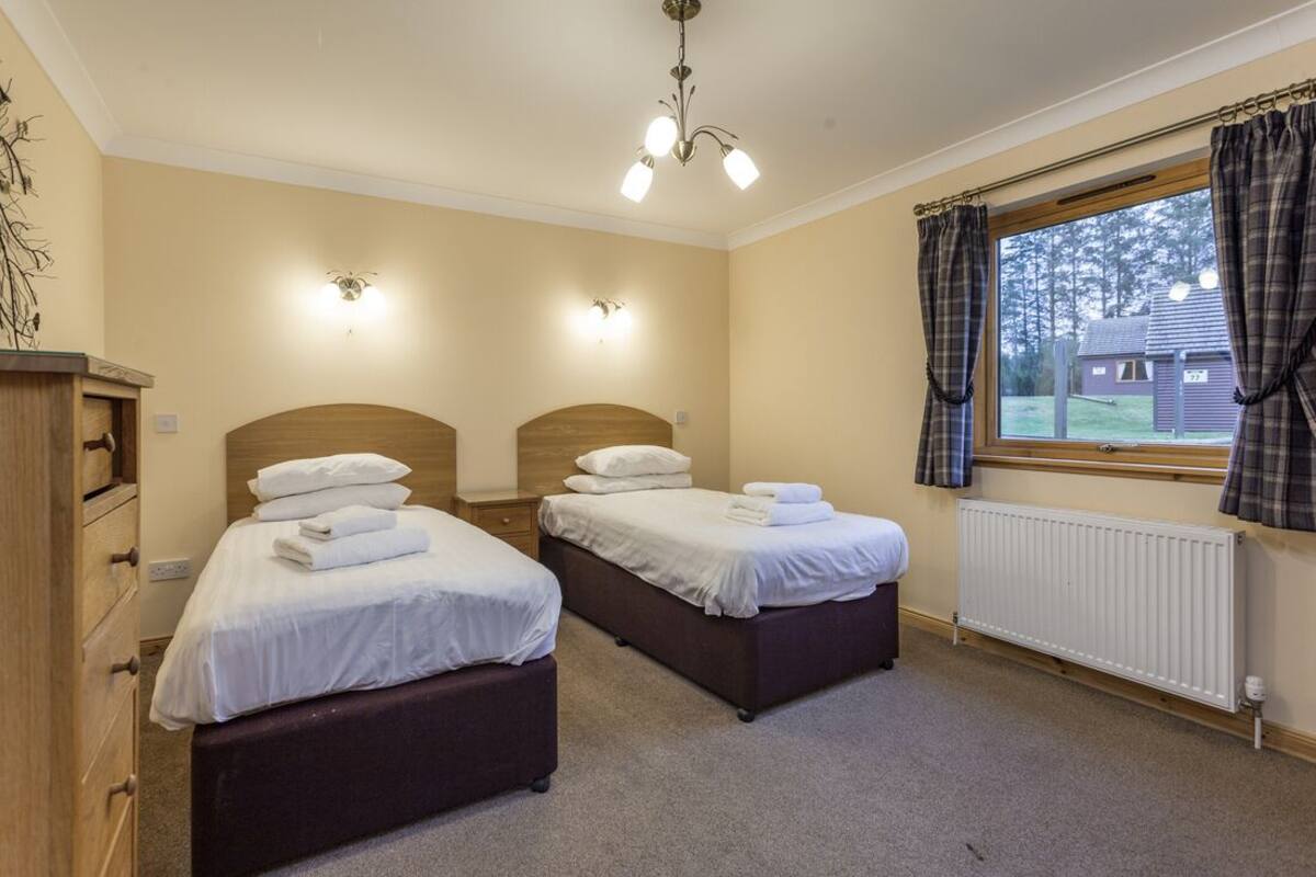A bedroom with two beds, a wooden dresser, a radiator, and a window with curtains.