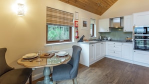 A modern kitchen with white cabinets, a wooden ceiling, and a dining area with a glass table and chairs.