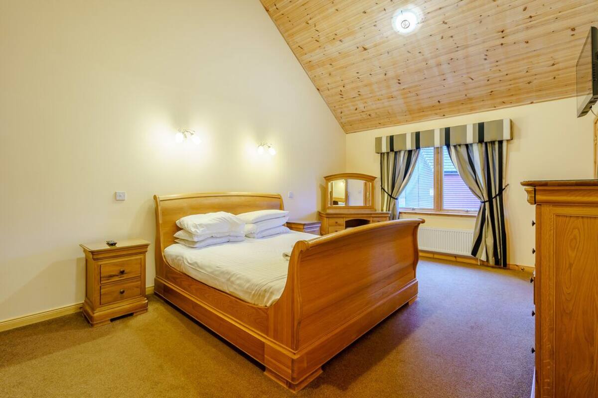 A bedroom with a wooden bed, bedside tables, a dresser, and a window with curtains.