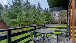 A wooden deck with a table and chairs, surrounded by a wooden fence and dense trees.
