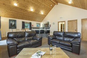 A spacious living area with two leather sofas, a wooden ceiling, and a kitchen in the background. - Landal Piperdam (Dundee)