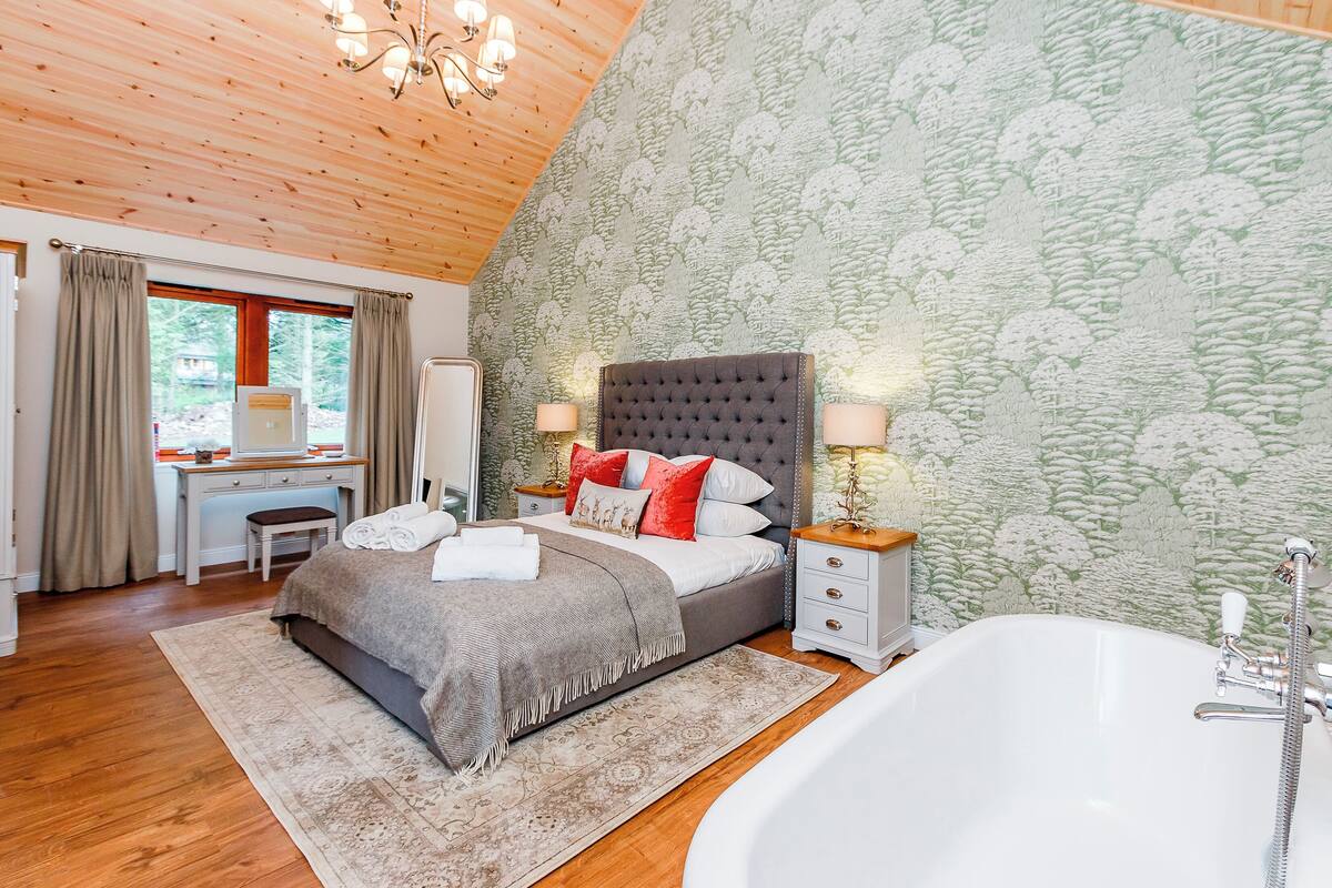 A bedroom with a bed, bedside tables, a desk, and a large window.