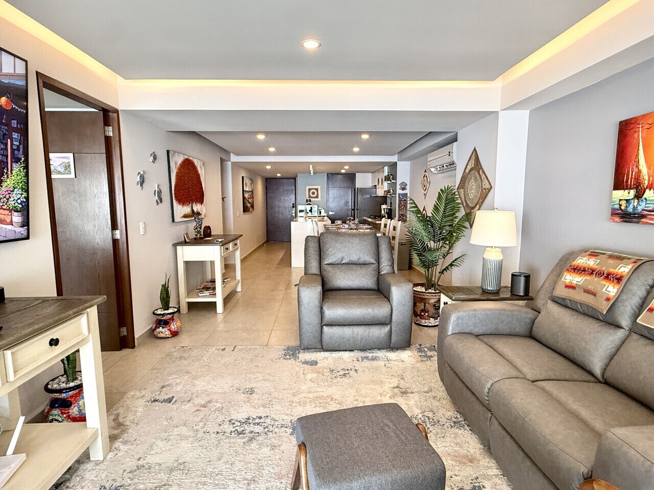 A modern living room with a grey sofa, a grey armchair, a coffee table, and a dining area in the background.