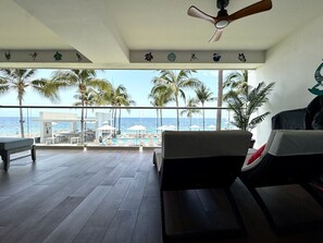 Ein Zimmer mit Meerblick, einem Deckenventilator und einem Poolbereich mit Liegen und Sonnenschirmen.