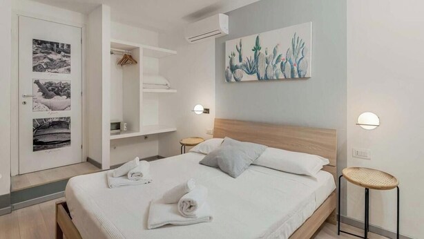 A modern hotel room with a neatly made bed, a wall-mounted cactus painting, and a wardrobe with hanging clothes. - Welcome to I Profumi del Mare, our guesthouse in the heart of La Spezia.We offer three spacious and tastefully furnished rooms, each with a private bathroom. Each room is an oasis of tranquility, and well designed to guarantee maximum comfort.The guestho (La Spezia)