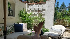 Un patio con un divano bianco, una panca in vimini e una sedia in metallo.