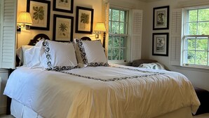 Un letto grande con biancheria bianca e cuscini decorativi, illuminato da due lampade fissate al muro.